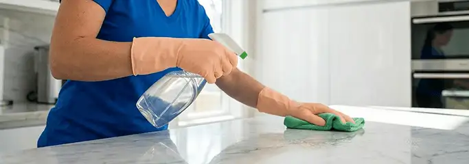 Maid service worker spraying and wiping a kitchen countertop with a microfiber cloth for sanitizing, Chattanooga, TN.