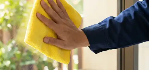 House cleaner wiping a glass window with a yellow microfiber cloth for streak-free cleaning, Chattanooga, TN.